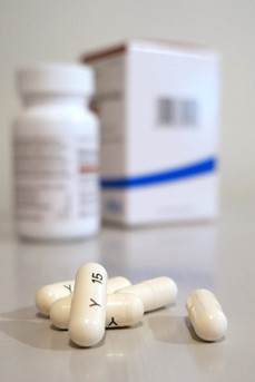 Des gélules blanches sont posées sur une table devant un flacon et une boite de médicaments