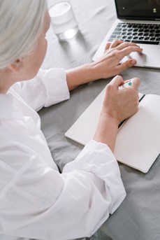 Une femme senior travaille sur ordinateur et écrit sur un cahier