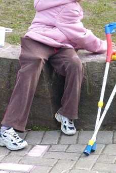 Une enfant en situation de handicap moteur joue à côté de ses béquilles