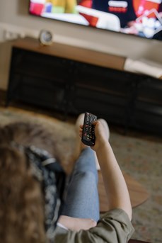 Une femme assise sur son canapé utilise une télécommande pour changer les chaines de sa télévision