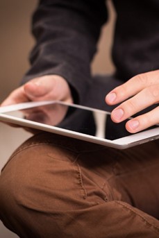 Un homme navigue sur internet avec sa tablette posée sur ses genoux