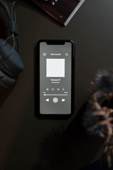 A côté d'un casque audio, un téléphone portable posé sur une table diffuse un podcast