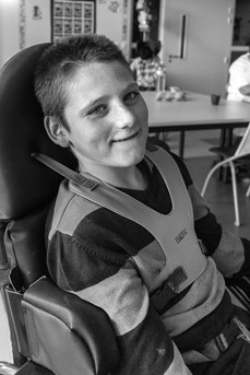 Un enfant polyhandicapé souriant est assis dans sa chaise roulante