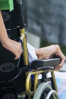 Une aide-soignante en EHPAD pousse le fauteuil d'une personne âgée dépendante