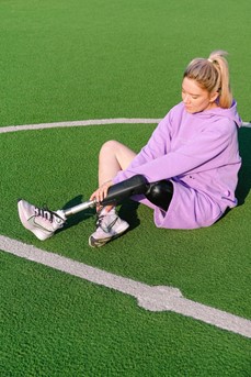 Une femme assise au milieu d'un terrain est équipée d'une prothèse à la jambe pour pratiquer son sport
