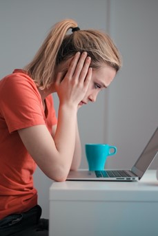 Une femme blonde se tient la tête dans les mains devant son ordinateur