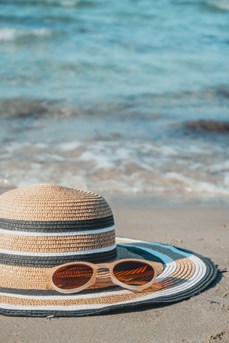 Un chapeau et des lunettes de soleil sont posés sur le sable d'une plage devant la mer