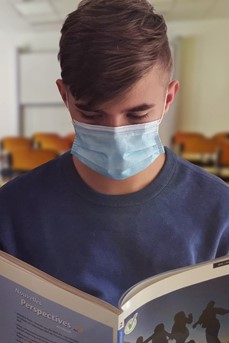 Dans une salle de cours, un étudiant portant un masque chirurgical lit un livre