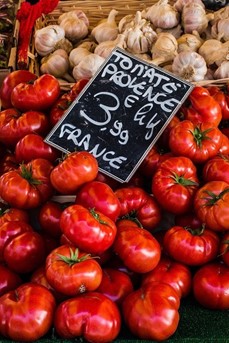 Une cagette de tomates de Provence, avec un panneau indiquant le prix au kilo, et des gousses d'ail