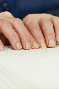 Les mains d'une personne aveugle parcourent un libre en braille