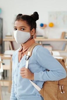 Une jeune élève avec un masque et son cartable se trouve dans sa salle de classe
