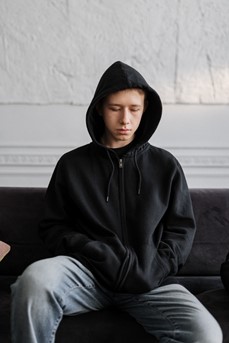 Une adolescent portant un sweat à capuche noir est assis sur un canapé pour parler de ses troubles psychiques