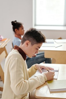 Dans une salle de classe, un écolier écrit dans un cahier assis à sa table