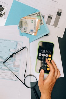 Une personne fait sa comptabilité avec une calculatrice avec sur une table des graphiques et une enveloppe avec des billets en euros