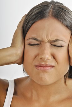 Une jeune femme avec une expression de douleur sur le visage se couvre les oreilles