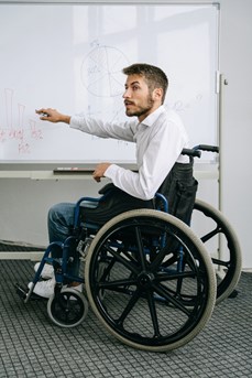 Un professeur en chaise roulante devant un tableau blanc